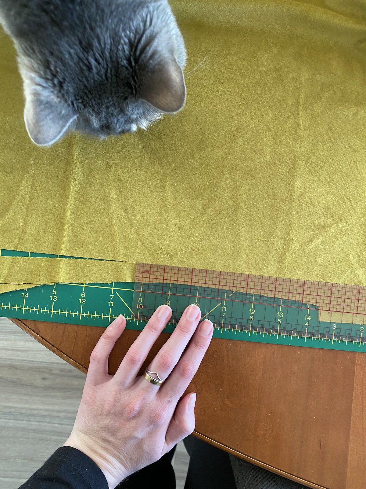 velvet fabric lays atop a green cutting mat being cut as a cat looks on 